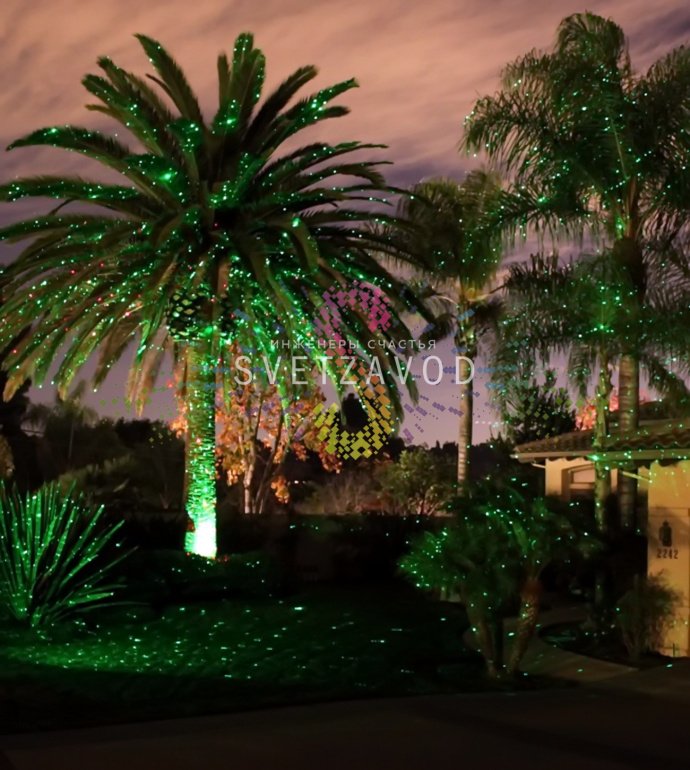 Лазерный проектор Garden X-30 Premium (X-38) в работе, создает зеленые и красные лазерные узоры анимации 'Светлячок' на стене, установлен на грунтовом основании.