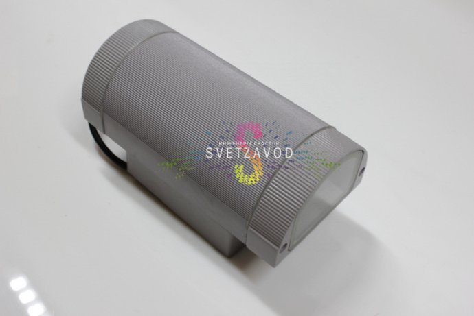 Крупный план двухстороннего светодиодного прожектора в сером металлическом корпусе с полукруглым рассеивателем, видна маркировка и крепление