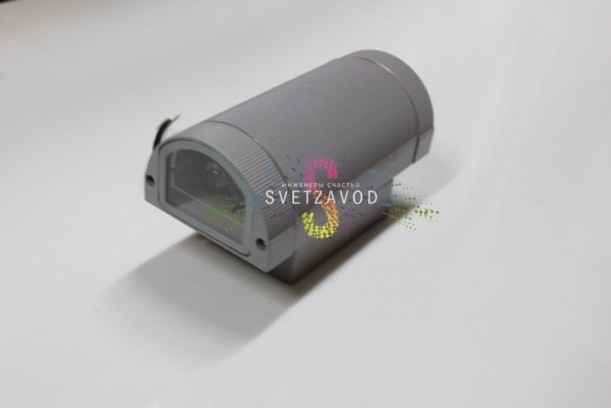 Крупный план двухстороннего светодиодного прожектора в сером металлическом корпусе с полукруглым рассеивателем, видна маркировка и крепление