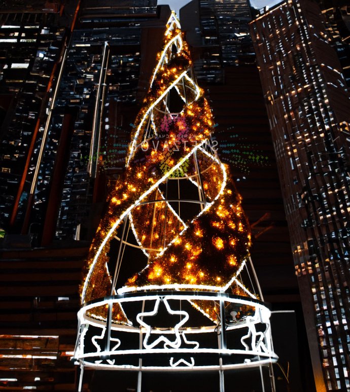 Крупный план светодиодной елки Конус с золотой мишурой, стальным каркасом и теплым белым свечением, установленной на улице.