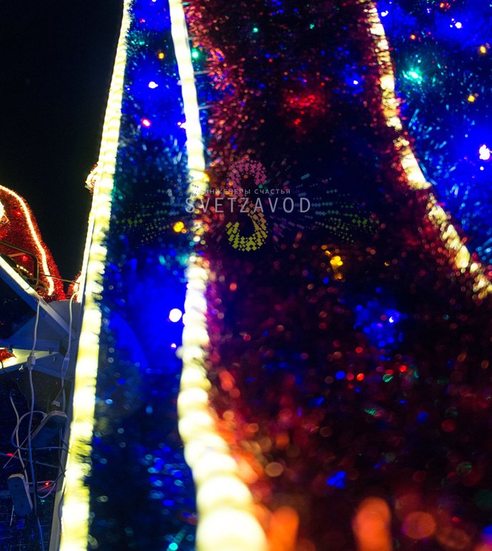 Детальное фото световой конструкции Подарок 300х300х400 см. Виден прочный стальной каркас, светодиодные гирлянды, мишура и бант. Конструкция предназначена для уличного использования.