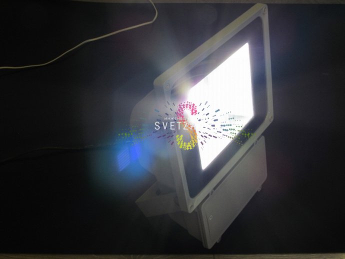 Светодиодный уличный прожектор мощностью 70Вт в сером металлическом корпусе с защитным стеклом, установленный на кронштейне для накладного монтажа.