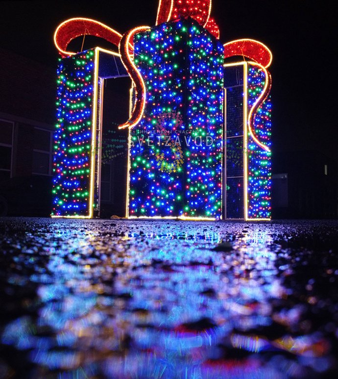 Детальное фото световой конструкции Подарок 300х300х400 см. Виден прочный стальной каркас, светодиодные гирлянды, мишура и бант. Конструкция предназначена для уличного использования.