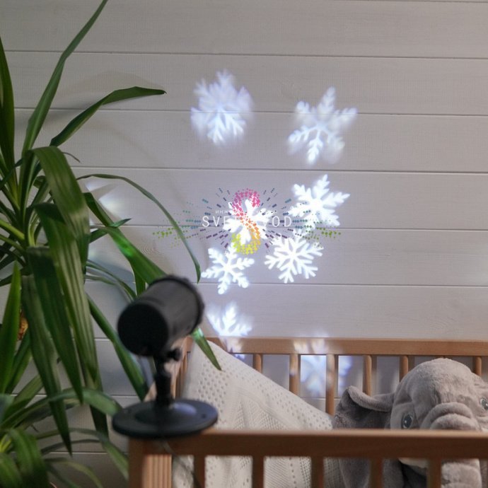 Черный светодиодный проектор Neon-Night на поверхности, проецирующий динамичные белые снежинки на стену или фасад здания.