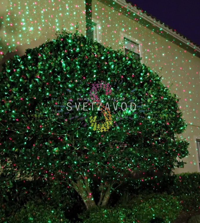 Лазерный проектор Garden X-30 Premium (X-38) в работе, создает зеленые и красные лазерные узоры анимации 'Светлячок' на стене, установлен на грунтовом основании.