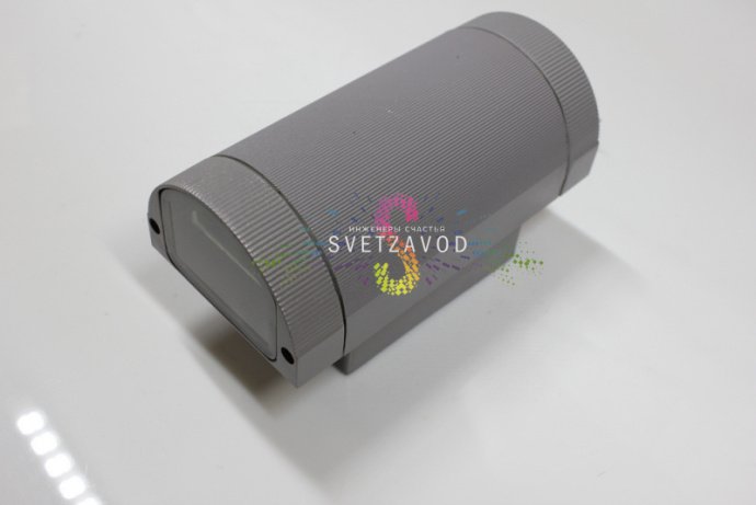 Крупный план двухстороннего светодиодного прожектора в сером металлическом корпусе с полукруглым рассеивателем, видна маркировка и крепление