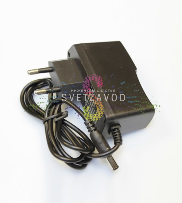 Детальное фото блока питания для гирлянды-роса: черный корпус, маркировка 220/12В 1A, входной и выходной разъемы, кабель.