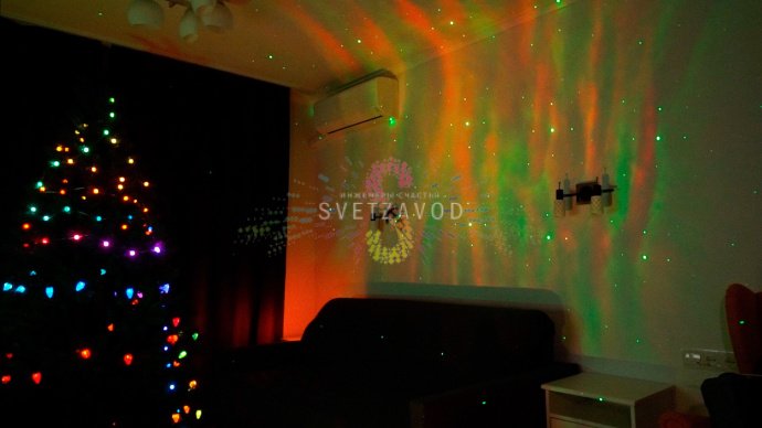 Лазерный проектор X-40 в работе: создает динамичную проекцию северного сияния и звезд на стене в темной комнате.