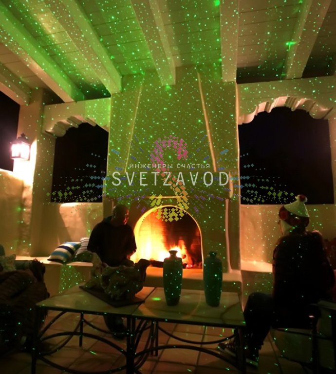 Лазерный проектор Garden X-30 Premium (X-38) в работе, создает зеленые и красные лазерные узоры анимации 'Светлячок' на стене, установлен на грунтовом основании.